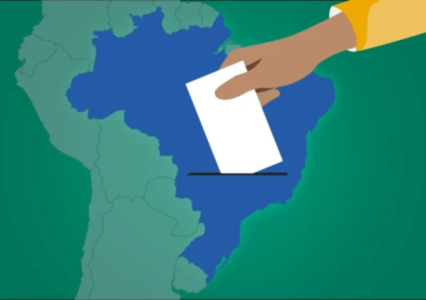 Ilustração de um mapa do Brasil em azul sobre fundo verde, visto de cima. Uma mão parda, vestindo manga amarela, aparece no canto superior direito, colocando um retângulo branco que representa uma cédula de votação sobre a área do mapa, simbolizando o ato de votar no país.