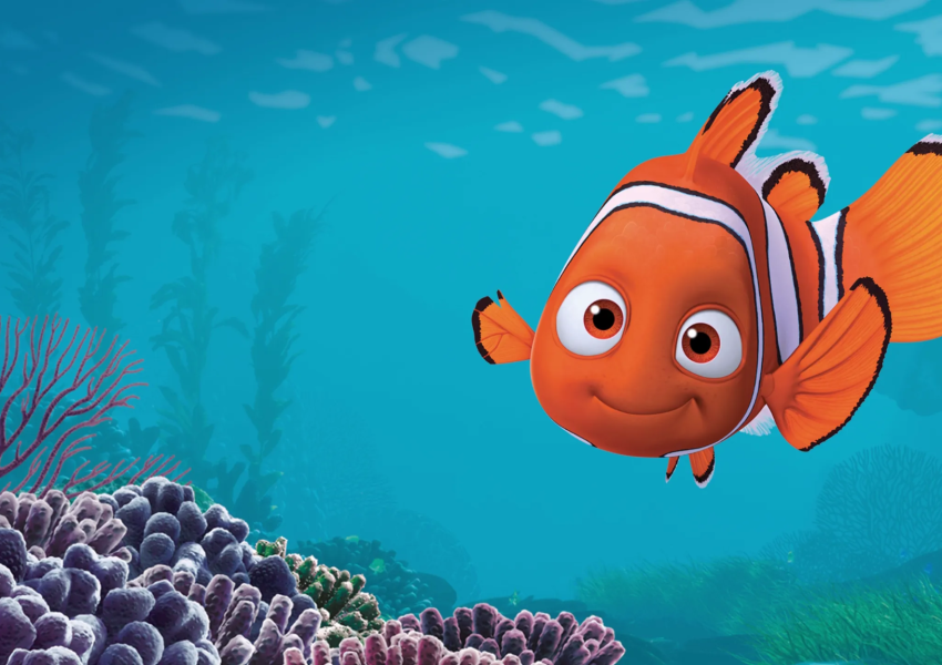 Imagem da animação Procurando Nemo. À direita da cena, Nemo aparece sorrindo levemente, com os olhos voltados para a frente. Sua nadadeira direita é visivelmente menor que a esquerda, característica que o diferencia ao longo da história. Ao fundo, vê-se um ambiente marinho em tons de azul. Na parte inferior da imagem há diferentes corais em tons de roxo, rosa e cinza, além de vegetação marinha ao fundo, desfocada, sugerindo profundidade. Reprodução/Pixar